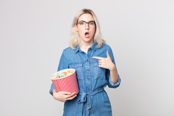 young pretty albino woman looking shocked and surprised with mouth wide open, pointing to self with...