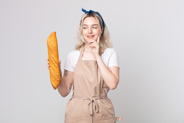 young pretty albino woman smiling happily and daydreaming or doubting with a bread baguette