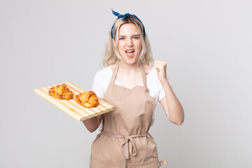 young pretty albino woman shouting aggressively with an angry expression with a croissants tray