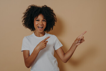 Young african american girl cheerfully smiling and pointing with index fingers up to side