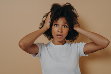 Worried stressed african female with open mouth holding head in hands isolated on beige background