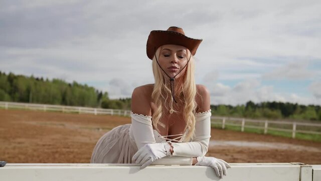 sexy blonde lady on ranch, woman is wearing cowboy hat and white romantic dress
