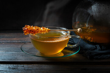 Hot steaming tea a glass cup with a stick of rock candy on a dark rustic wooden table, copy space, selected focus