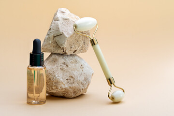 Beauty cosmetic facial roller, cosmetic bottle of essential oil on beige background with natural stones. Front view, copy space. Natural skincare products concept.