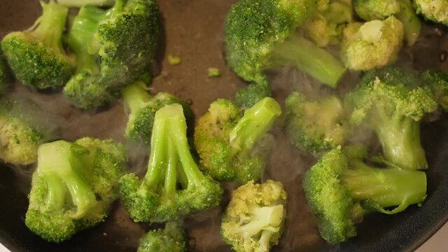 Skillet full of freshly cut broccoli cooking on the stove top - slow motion