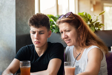 A woman and her teenage son look at the menu together in a cafe and choose food and drinks, they laugh, communicate and discuss the guy's future, his studies, relationships with people