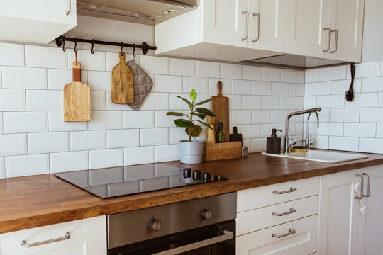 Kitchen brass utensils, chef accessories. Hanging kitchen with white tiles wall and wood tabletop.Green plant on kitchen background