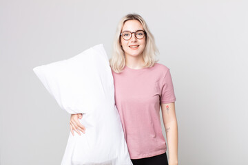 young pretty albino woman looking happy and pleasantly surprised wearing pajamas and holding a...