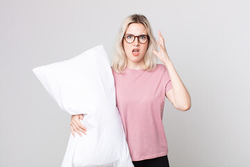young pretty albino woman screaming with hands up in the air wearing pajamas and holding a pillow