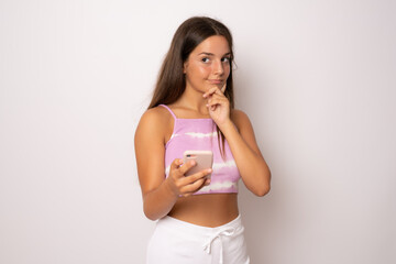 Pensive young girl using smartphone in summer clothing isolated over white background.