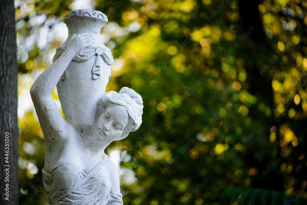 Wall mural sculpture of a girl in the spring park. An old statue in a park of a sensual semi-nude Greek or Italian Renaissance woman with a vase in a city park. sunny day in the summer garden. close-up