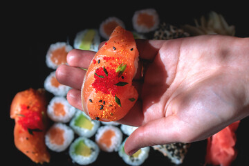 The girl holds a large sushi in the palm of her hand against the background of a set with rolls.