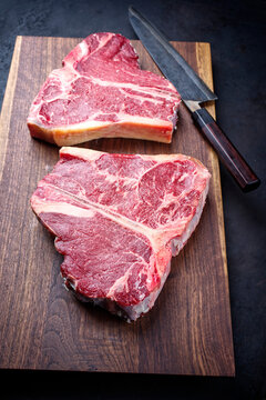 Two raw dry aged wagyu porterhouse beef steaks offered as close-up on modern design wooden board with a Japanese gyuto knife