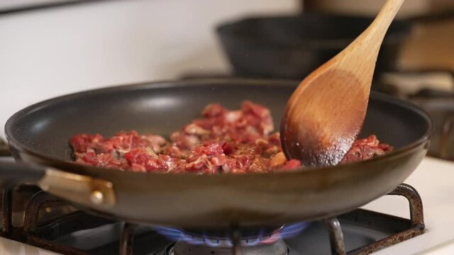 Stirring small pieces of beef searing and sizzling in a hot pan and oil on the stove - isolated close close up slow