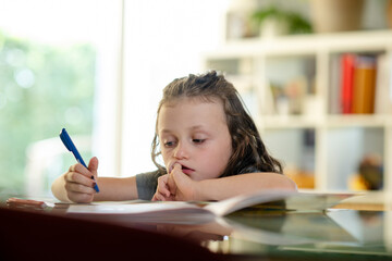 Mädchen, 6, sitzt unkonzentriert bei der Hausaufgabe