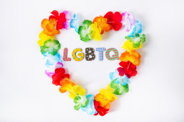 Hawaiian flower necklace in the shape of a heart with LGBTQ inscription inside on the white background. LGBTQ concept with rainbow flag colors. Pride month. Selective focus.