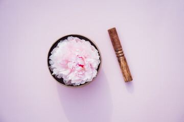 Top view Tibetan singing bowl with floating in water pink peony inside and special stick on pink background. Meditation and Relax. Exotic massage. Minimalism. Direct sunlight and shadows.Copy space.