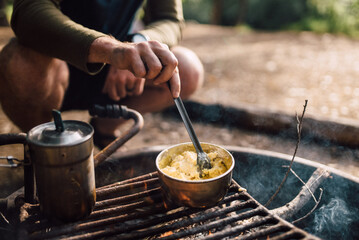 Man Cooking Simple, Healthy Breakfast Scrambled Eggs at Campground Over the Fire While Camping Outside Recreation