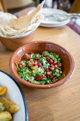 Close-up of a tasty tabbouleh salad with pomegranate seeds in a brown ceramic bowl