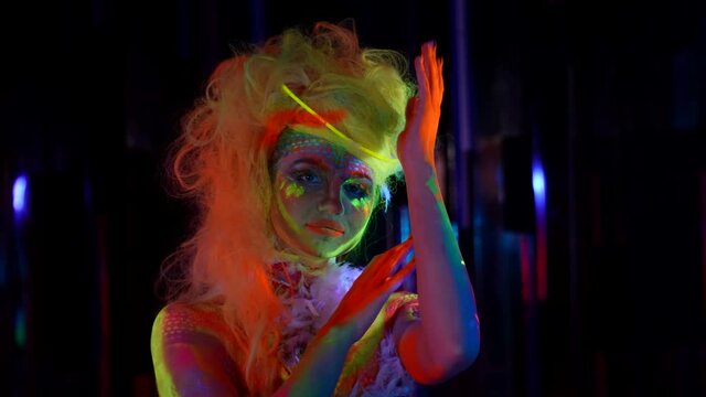 beautiful actress with fluorescent makeup is posing for camera at darkness, medium portrait shot