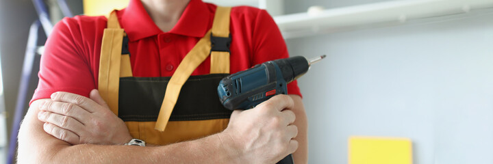 A man in work clothes holds a screw gun - obrazy, fototapety, plakaty