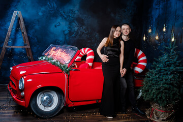 Obraz na płótnie Canvas Young happy couple man and woman in love in Christmas are hugging near a red retro car with New Year's gifts. Kiss, girl, happiness, quarantine Christmas celebration, holiday.