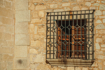 Wooden window with wrought iron grid on the stone facade of gothic building, in a sunny day at Caceres. A fully preserved medieval town in Spain.