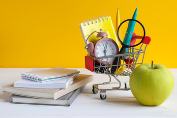 Back to school concept. Grocery cart with school supplies, green apple, note pads and books on the table. School shopping