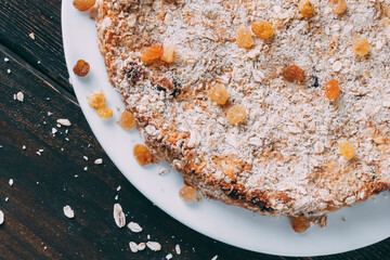 Round shaped oat cake on a wooden table. Sprinkle with raisins and cereal. Piece of cake from the corner