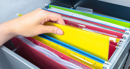 Hand pick yellow hanging file folder from open drawer. Administration clerk finding paperwork from office storage. Corporate information record, organized category and database management concept. - obrazy, fototapety, plakaty
