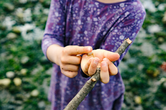 Closeup of a young girl holding a stick and a shell on the beach