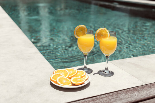 Glass with orange juice near the pool