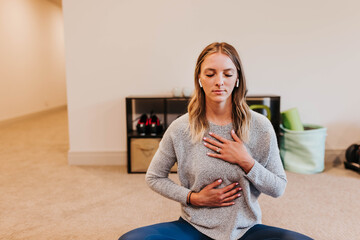 Woman wears earbuds while meditating in her home gym