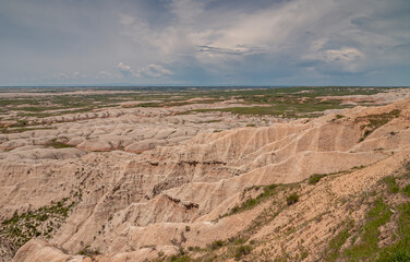 Badlands National Park, SD, USA - June 1, 2008: Bad weather cloudscape approacing over beige geological deposits with green prairie on horizon. - obrazy, fototapety, plakaty