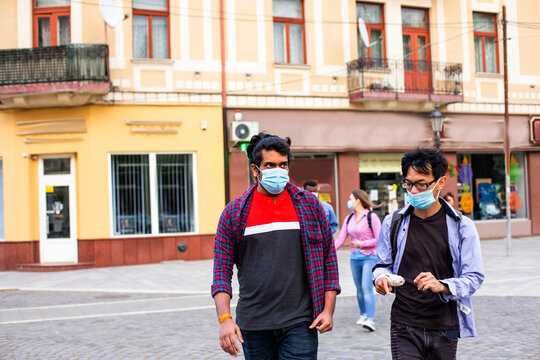 Two young multiracial friends in masks chatting outdoors