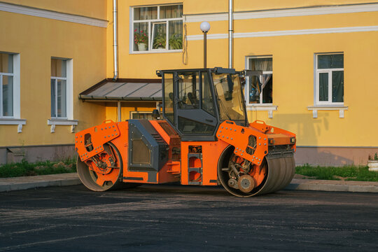 Orange road vibration roller stands on the new asphalt square in the city. Evening, sunset.