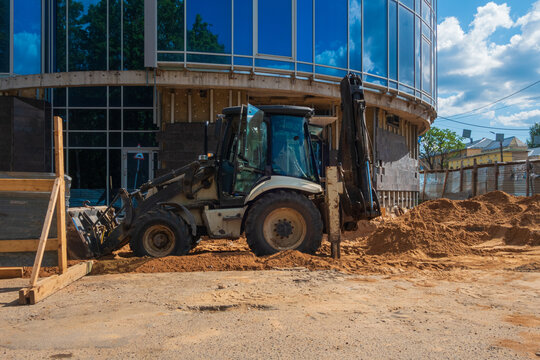 A modern tractor stands on the sand near a glass building under construction.