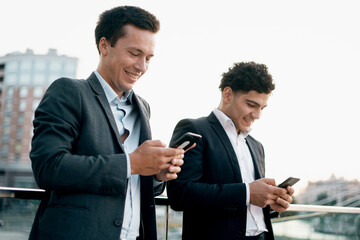 Successful colleagues work together on a social network. Businessmen young people work near the office in business suits holding gadgets in their hands. They are discussing a new startup project.