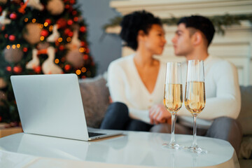 They drink champagne in glasses and communicate with friends on a social network. A young couple, a man and a woman, celebrate the New Year and Christmas online.