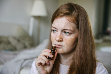 Young woman is sniffing essential oil. Loss of smell and taste from Covid - obrazy, fototapety, plakaty