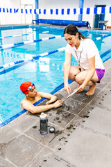 latin swimming woman coach talking some advices to young disabled man in pool in disability concept...
