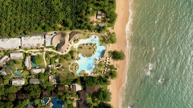 Relaxing sea waves on a hotel beach. Aerial view of small ocean waves on a paradise sand beach near big blue pool. Sea waves create vacation mood. People relax travel vacation fun concept.