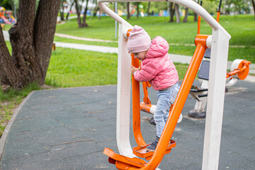 Fototapeta premium Girl doing exercises on the outdoor exercise machines FEET BREEDING resting their legs. Easy-to-use cardiovascular fitness equipment at sports ground in the city park