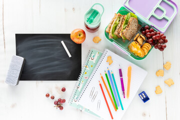 Top down view of an assortment of school supplies and lunch along with a blank chalkboard, chalk...