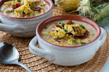 Close up view of a soup crock filled with chicken and corn chowder topped with grilled corn, ready...