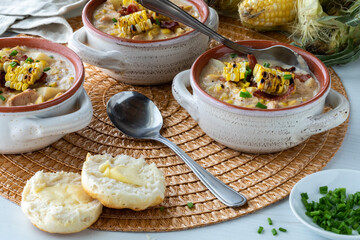 Three bowls of chicken and corn chowder soup served with biscuits, ready for eating.
