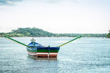 Fototapeta premium Fishing boat with oars in the sea in front of the wooden pier. Cananéia, Brazil. Caiçara culture.