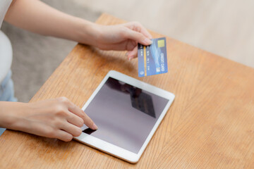 Closeup hand of young asian woman holding credit card shopping online with tablet computer blank display screen buying and payment, girl using debit card purchase or transaction, e-commerce concept.