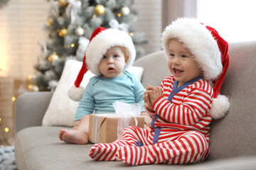 Obraz na płótnie Canvas Cute children in Santa hats sitting on sofa at home. Christmas celebration