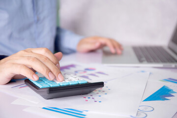 Fototapeta premium Hands of businessman calculate tax with calculator while laptop computer on desk, man planning finance and investment with graph and chart, statistic and examining account, business concept.